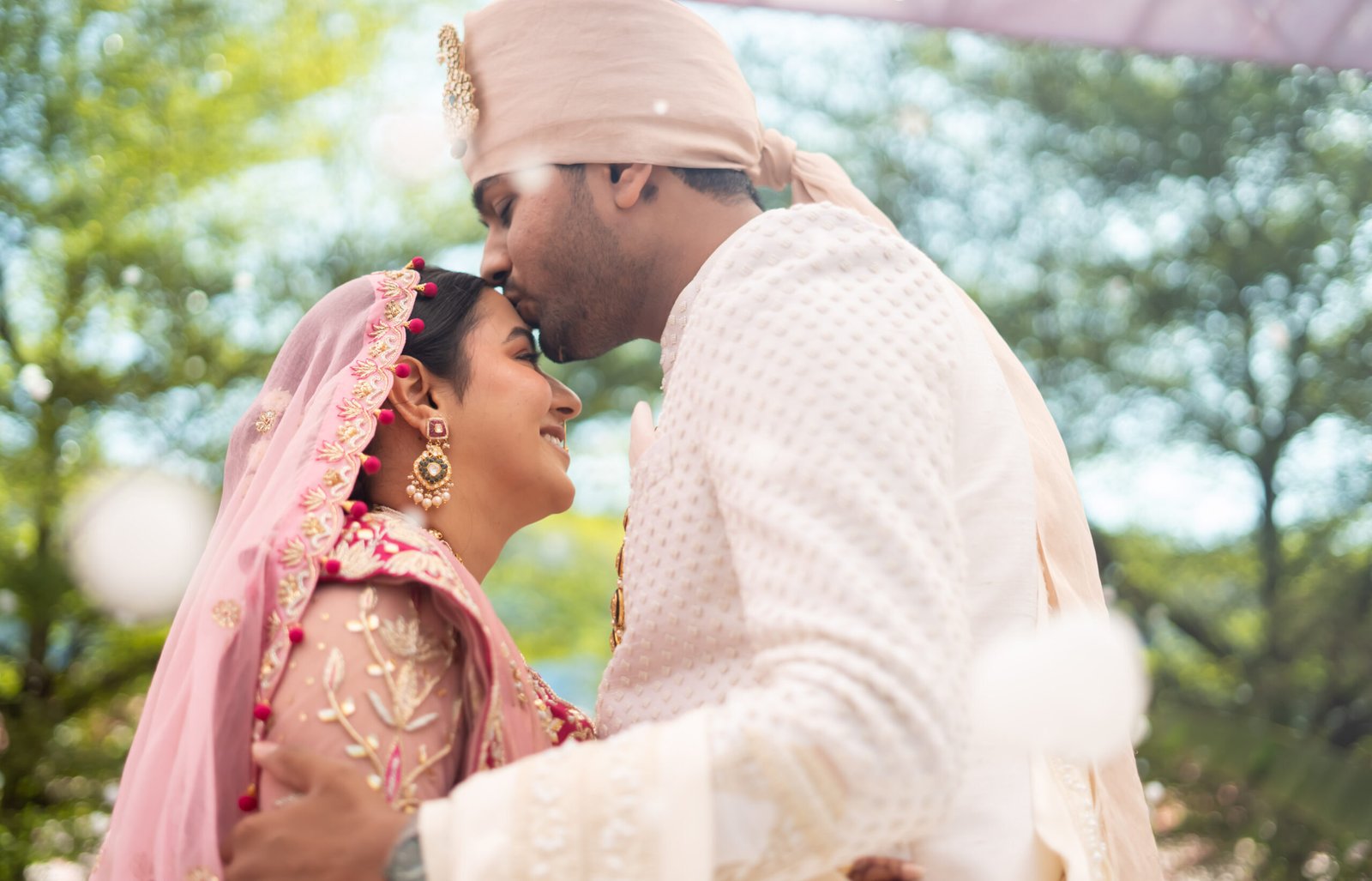 Groom kissing bride's forehead during an intimate outdoor wedding moment.