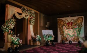 Floral wedding entrance decor with pastel drapes, wooden frames, and a butterfly-themed floral backdrop by Milaap Weddings.