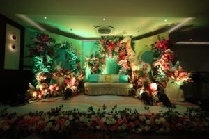 A whimsical wedding setup with a colorful floral arrangement, featuring a giraffe and rabbit statue on either side of a cozy sofa, under soft green lighting.