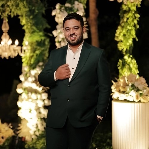 Ankit Makwana, director, posing confidently in a dark green suit at a floral-lit evening event