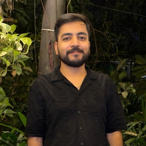 Akshay smiling in black shirt standing in a lush green garden at night