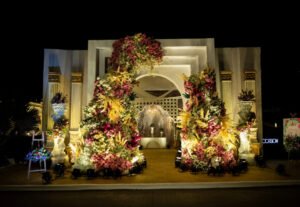 Floral wedding entrance arch with vibrant flowers and elegant lighting.