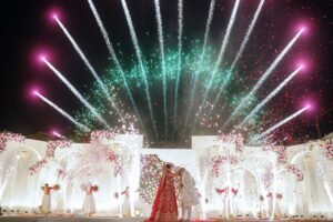 Bride and groom kissing with fireworks and flower petals falling during their wedding.