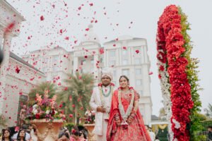 bride and groom standing under flower arch with rose petals showering